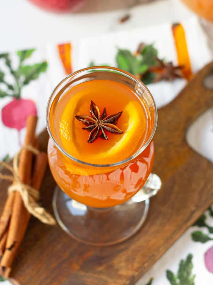 Apple cider in a clear glass garnished with orange slices and star anise.