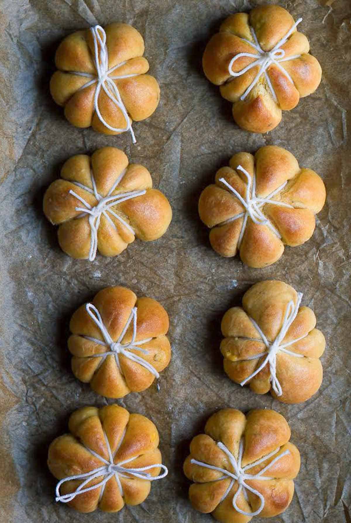 8 baked pumpkin bread rolls tied with twine in pumpkin shape.