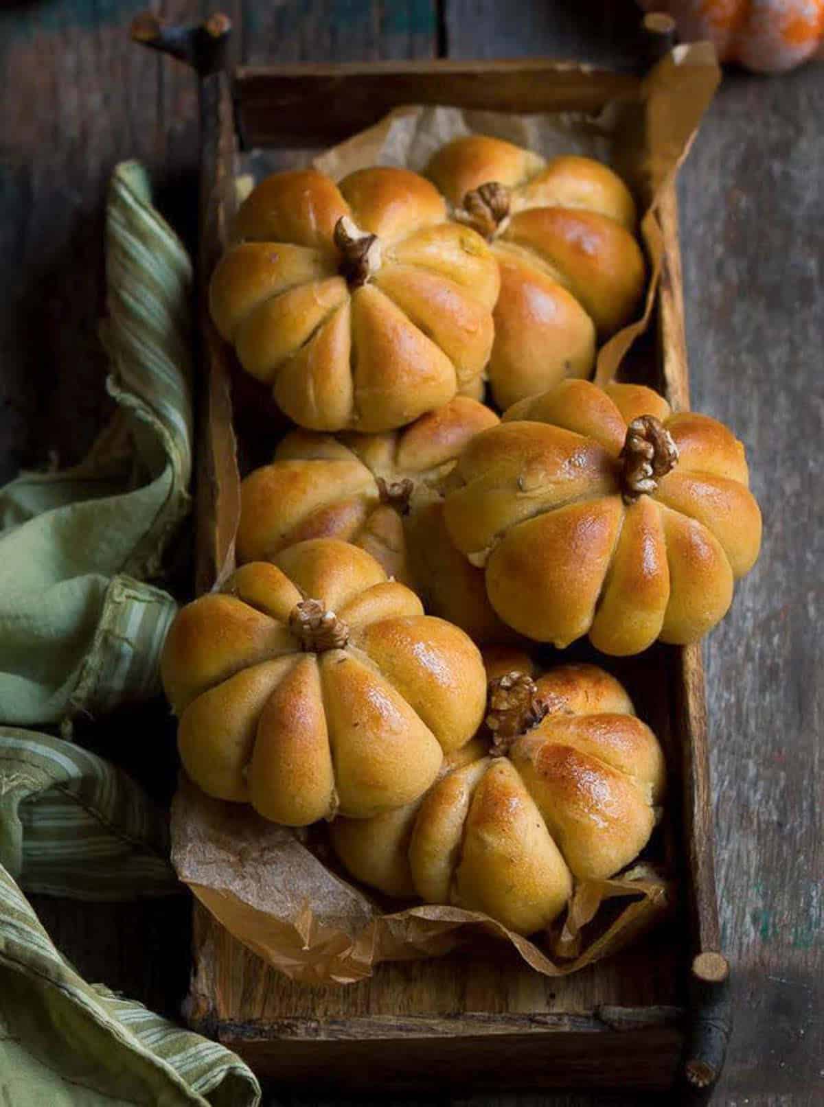 Pumpkin bread rolls in a small wooden tray with a green napkin.