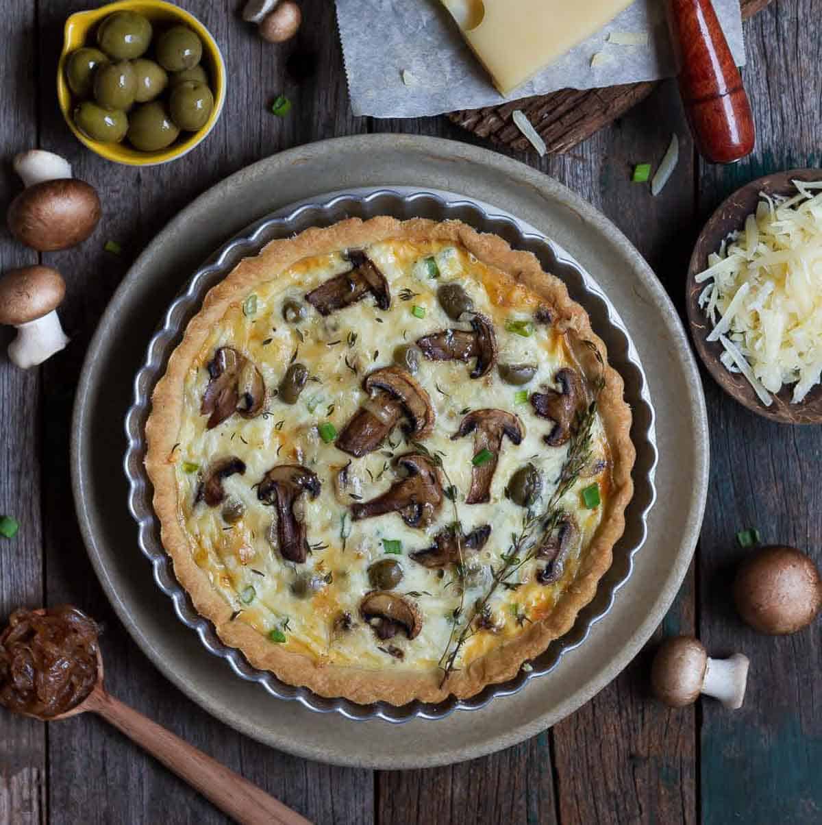 mushroom quiche on a platter with ingredients all around.