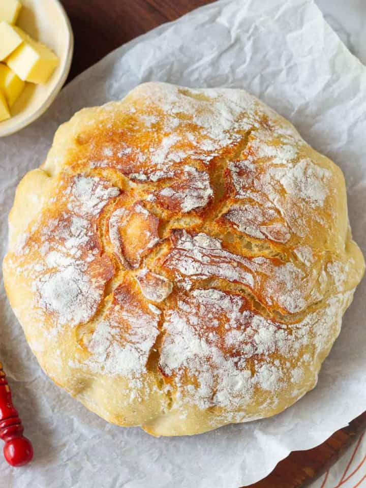 no knead Dutch oven bread on parchment paper with butter and butter knife.